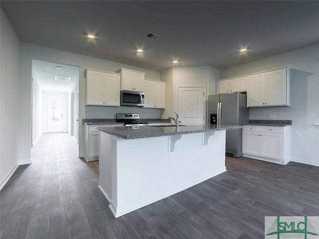 kitchen with appliances with stainless steel finishes, dark wood finished floors, white cabinets, a center island with sink, and baseboards