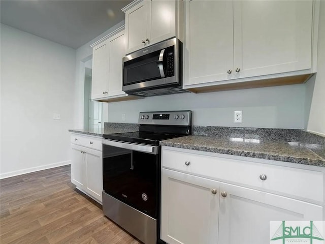 kitchen with stainless steel appliances, light wood-style flooring, dark stone countertops, baseboards, and white cabinetry