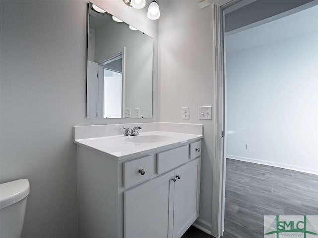bathroom with vanity, toilet, wood finished floors, and baseboards