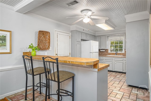 2014 Colonial Dr, Savannah, GA 31406 - kitchen featuring freestanding refrigerator, a peninsula, a kitchen bar, ceiling fan, and tasteful backsplash