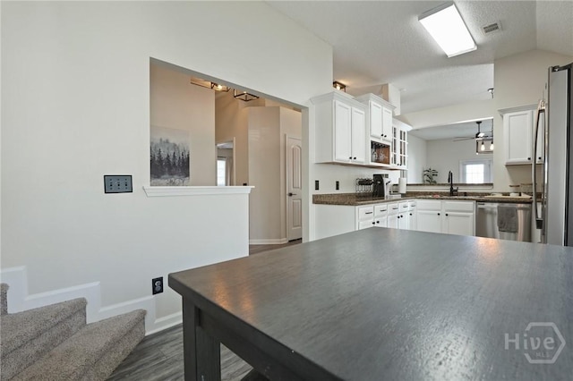 kitchen with lofted ceiling, appliances with stainless steel finishes, white cabinetry, dark wood-style floors, and dark countertops