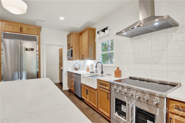 kitchen with built in appliances, wall chimney exhaust hood, a sink, dark wood finished floors, and tasteful backsplash
