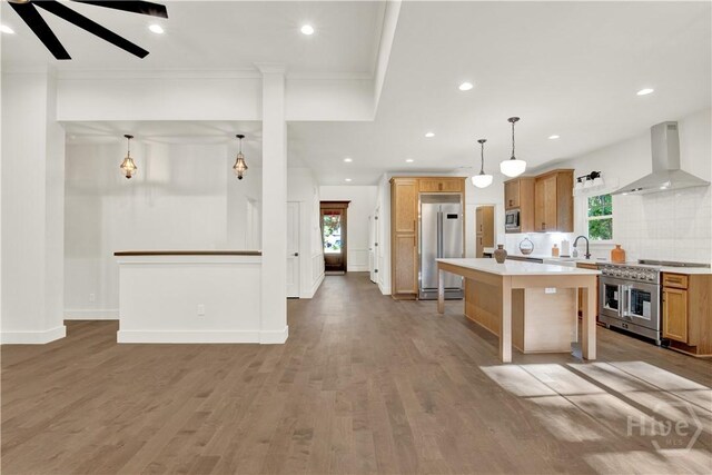 kitchen featuring wall chimney exhaust hood, built in appliances, light countertops, plenty of natural light, and crown molding