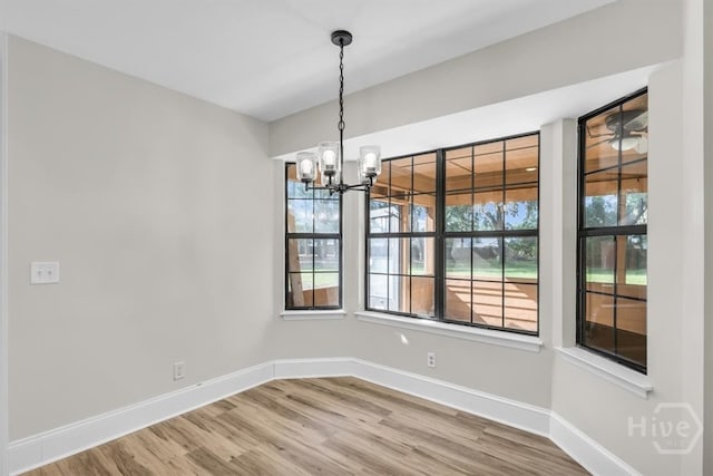 unfurnished dining area featuring a chandelier, baseboards, and wood finished floors