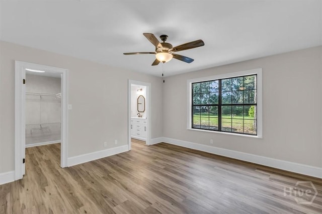 unfurnished bedroom featuring wood finished floors, a spacious closet, baseboards, a closet, and ceiling fan