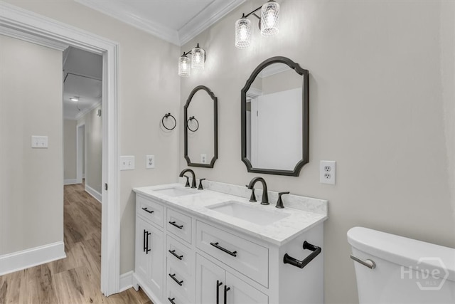 bathroom featuring crown molding, wood finished floors, double vanity, baseboards, and toilet