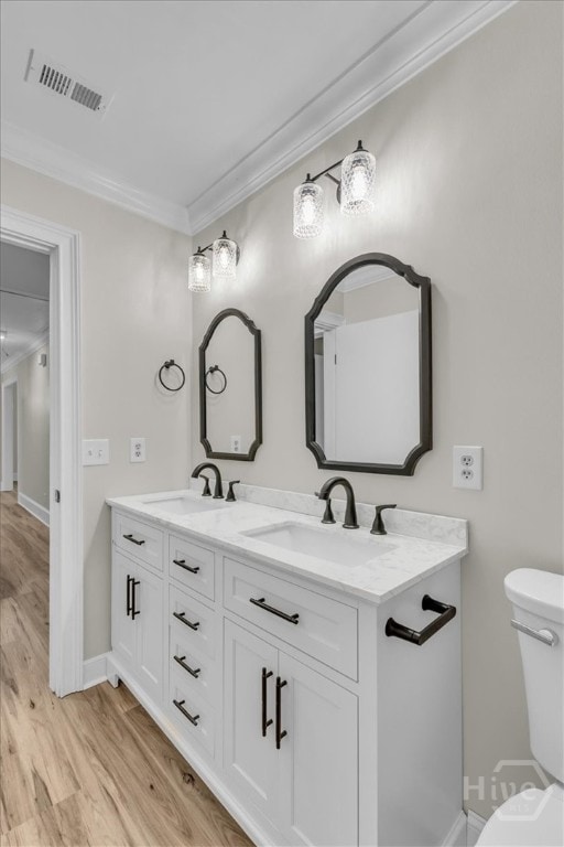 bathroom featuring ornamental molding, toilet, wood finished floors, double vanity, and baseboards