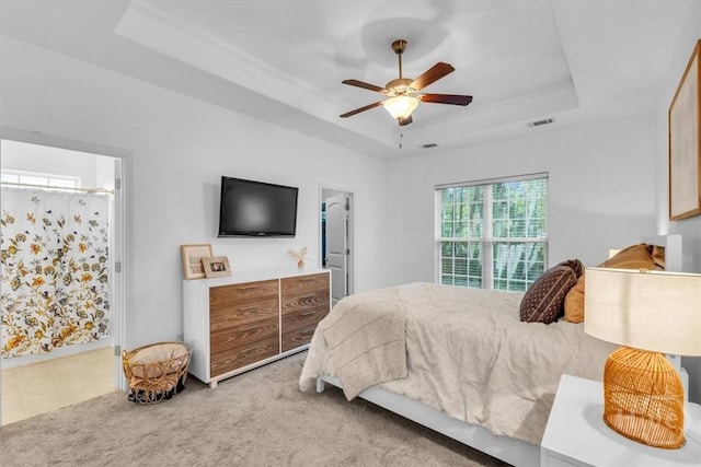 carpeted bedroom featuring a tray ceiling, ensuite bathroom, and ceiling fan