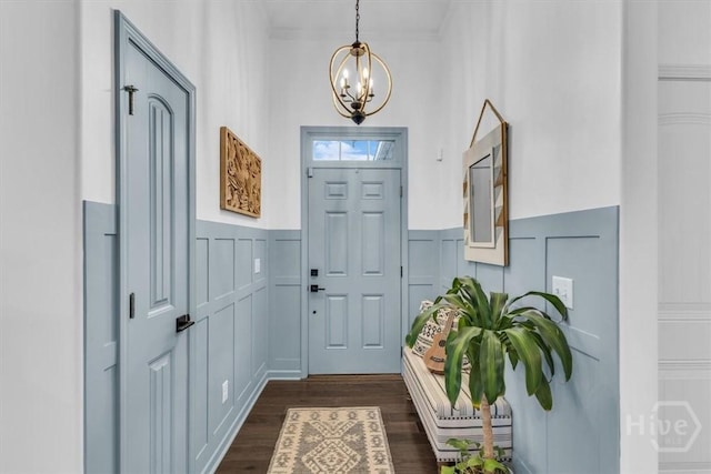 entrance foyer with a decorative wall, a chandelier, a wainscoted wall, dark wood-style flooring, and ornamental molding
