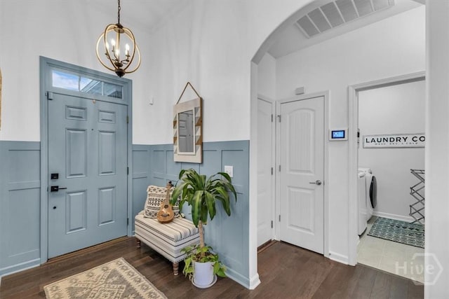 entrance foyer with washer and dryer, arched walkways, a chandelier, wainscoting, and dark wood-style floors