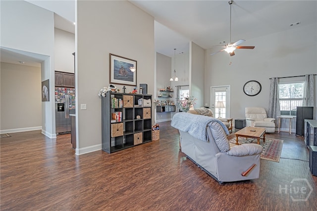 living room with a towering ceiling, dark wood-type flooring, ceiling fan, and baseboards