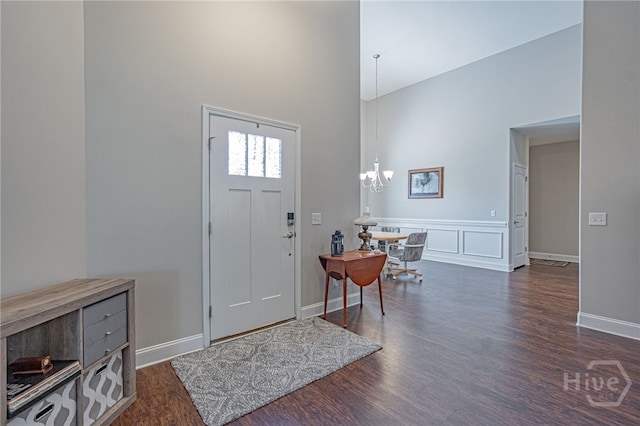 entryway with a towering ceiling, wood finished floors, a chandelier, baseboards, and a wainscoted wall