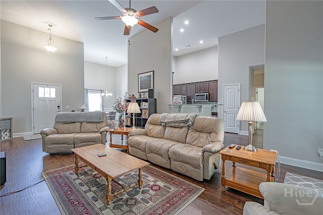 living area featuring high vaulted ceiling, a ceiling fan, baseboards, dark wood finished floors, and a chandelier