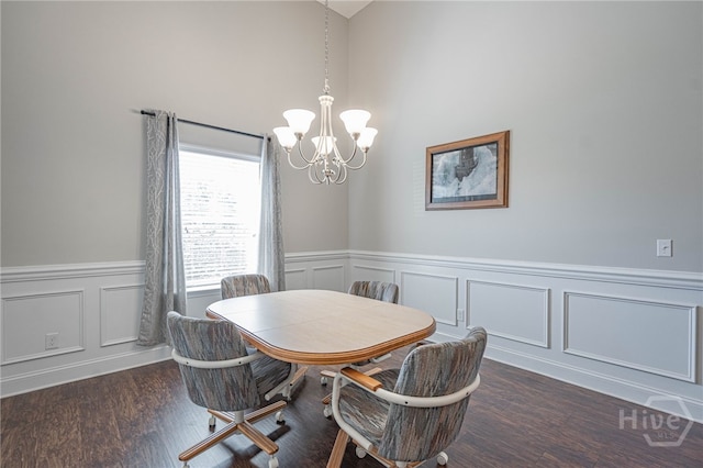 dining space with a chandelier, a wainscoted wall, a decorative wall, wood finished floors, and a towering ceiling