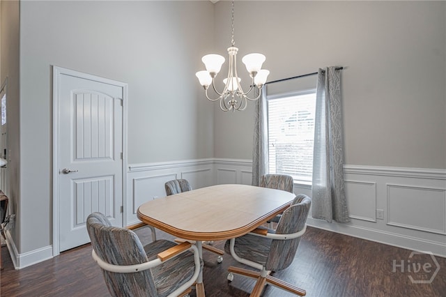 dining room with a chandelier, a high ceiling, wainscoting, a decorative wall, and dark wood-style flooring