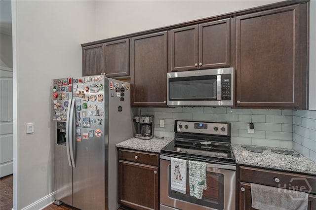 kitchen with appliances with stainless steel finishes, dark brown cabinets, tasteful backsplash, and light stone counters