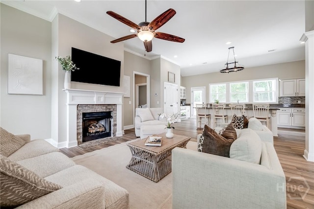 living area with ornamental molding, ceiling fan, a stone fireplace, recessed lighting, and light wood finished floors