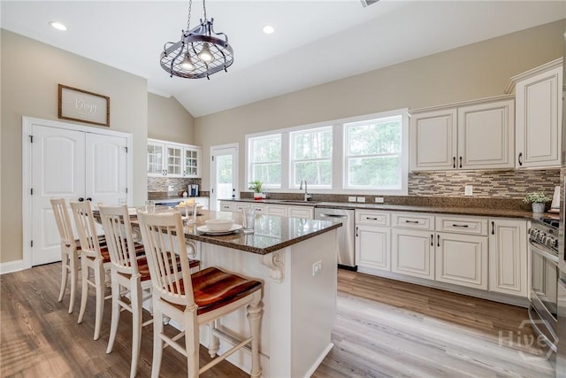 kitchen featuring appliances with stainless steel finishes, vaulted ceiling, decorative backsplash, light wood-type flooring, and a breakfast bar