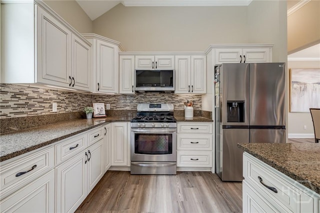 kitchen with appliances with stainless steel finishes, lofted ceiling, white cabinets, decorative backsplash, and dark stone counters