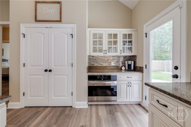 kitchen with oven, light wood-type flooring, white cabinetry, glass insert cabinets, and vaulted ceiling
