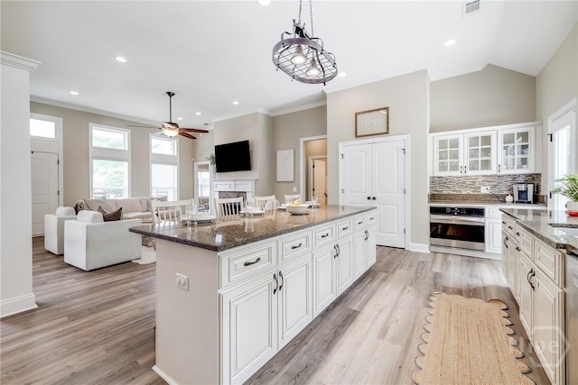 kitchen featuring stainless steel oven, ceiling fan, glass insert cabinets, a fireplace, and dark stone countertops