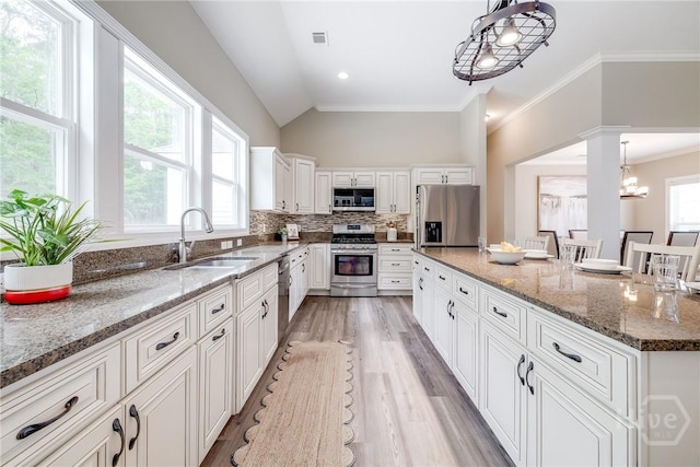 kitchen featuring appliances with stainless steel finishes, a sink, lofted ceiling, light wood-style floors, and white cabinetry