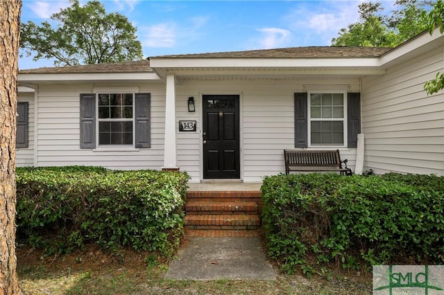 entrance to property with a porch and a shingled roof