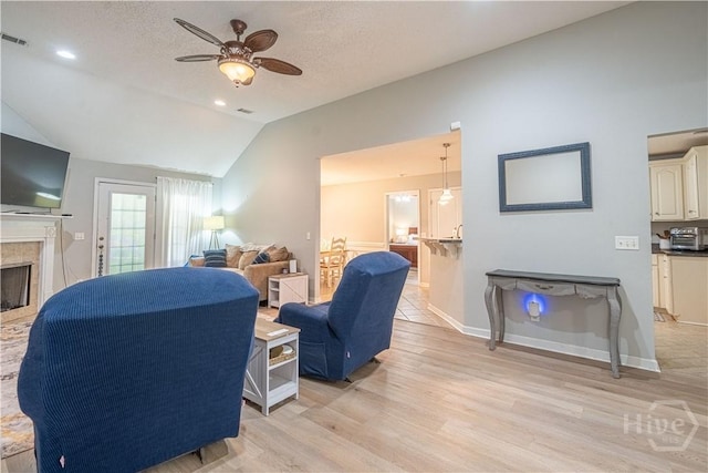 living area featuring a ceiling fan, vaulted ceiling, light wood-style flooring, a tile fireplace, and baseboards