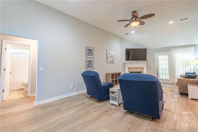 living room featuring vaulted ceiling, a fireplace, a ceiling fan, light wood-type flooring, and baseboards