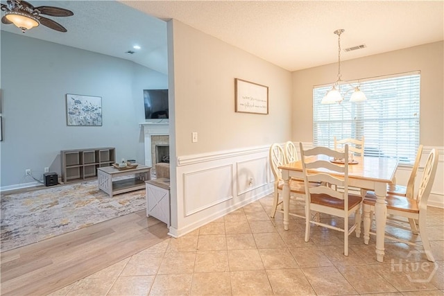 dining space featuring ceiling fan, a wainscoted wall, a tile fireplace, a decorative wall, and lofted ceiling