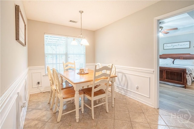 dining space with a decorative wall, light tile patterned floors, wainscoting, and ceiling fan