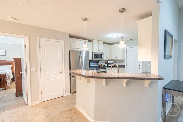 kitchen featuring stainless steel appliances, a peninsula, a breakfast bar, white cabinets, and a textured ceiling