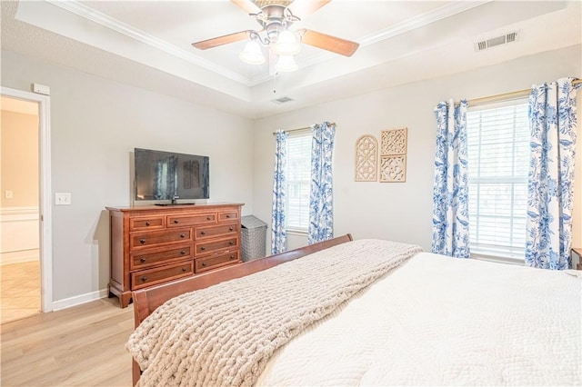 bedroom with crown molding, light wood-type flooring, a tray ceiling, ceiling fan, and baseboards