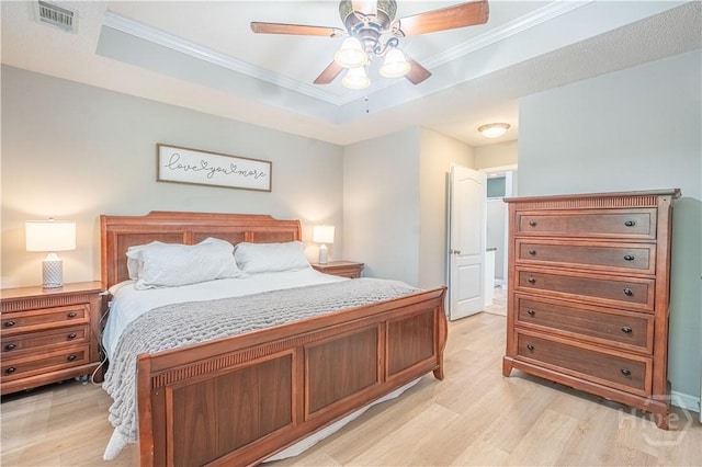 bedroom with light wood-style flooring, crown molding, a raised ceiling, and a ceiling fan