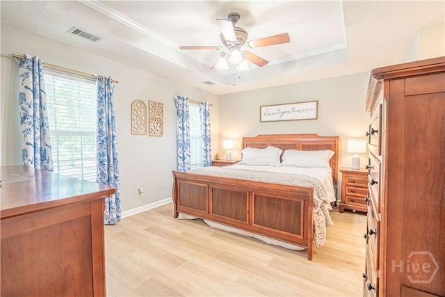 bedroom with a tray ceiling, light wood finished floors, baseboards, crown molding, and ceiling fan