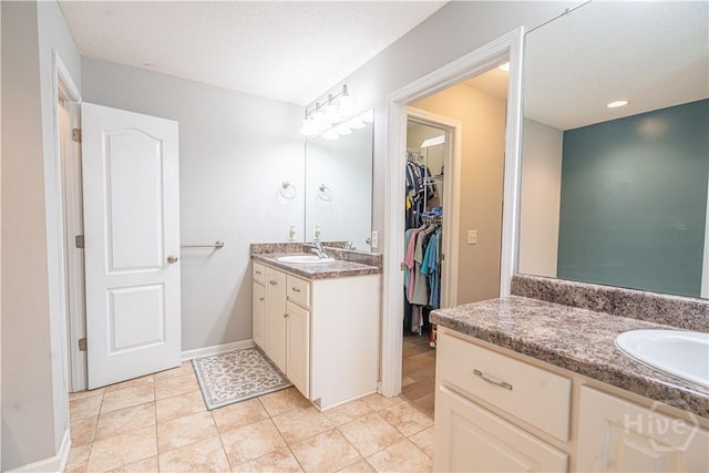 full bath featuring two vanities, a spacious closet, tile patterned flooring, and baseboards