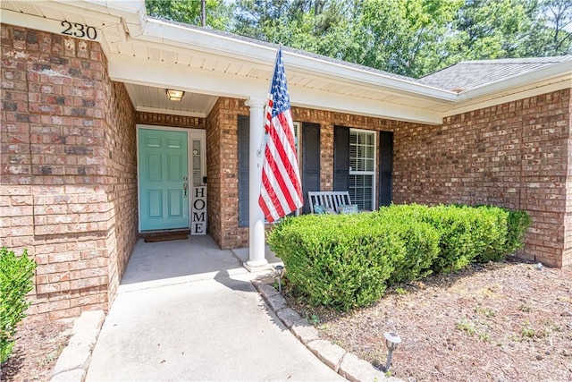 view of exterior entry with brick siding and covered porch