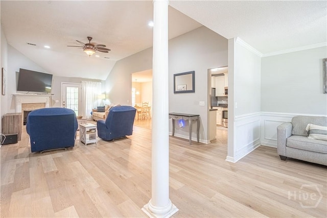 living area featuring ornate columns, a ceiling fan, light wood-type flooring, vaulted ceiling, and a fireplace