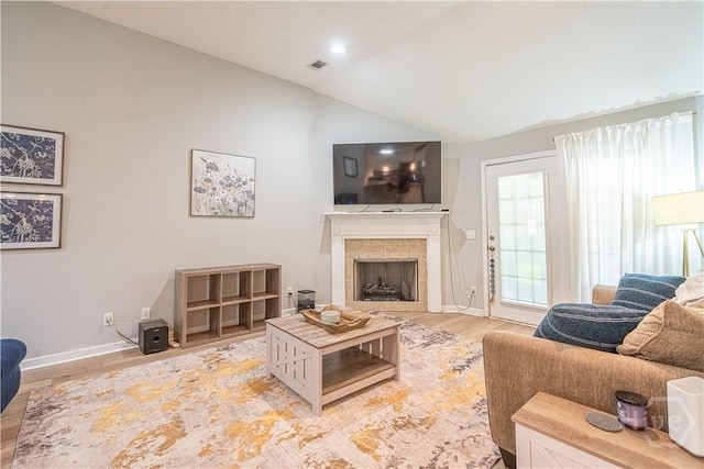 living area featuring vaulted ceiling, a tiled fireplace, light wood-style floors, and baseboards