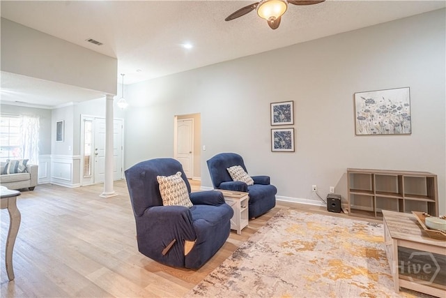 living area featuring a ceiling fan, light wood-type flooring, and decorative columns