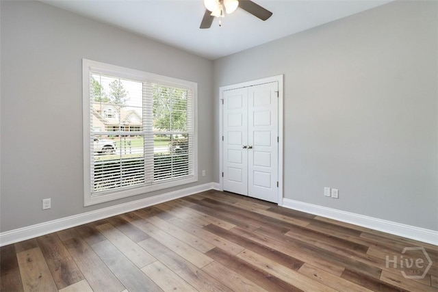 unfurnished bedroom with baseboards, wood finished floors, a closet, and a ceiling fan