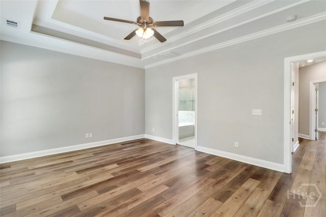 empty room featuring a raised ceiling, ceiling fan, hardwood / wood-style floors, ornamental molding, and baseboards