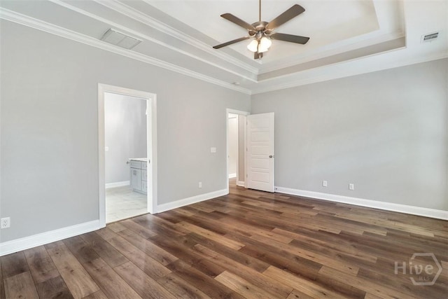 unfurnished bedroom with a raised ceiling, wood finished floors, crown molding, connected bathroom, and baseboards