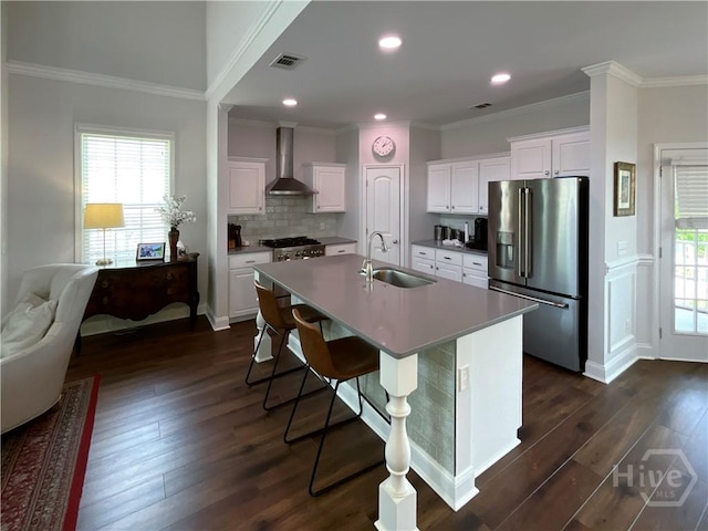 kitchen featuring appliances with stainless steel finishes, a sink, wall chimney exhaust hood, an island with sink, and dark wood-style flooring