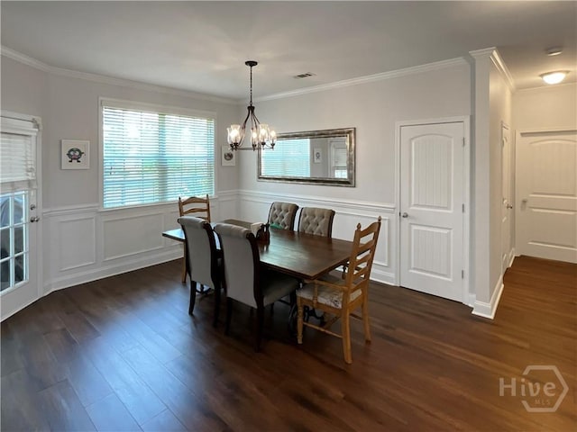 dining space with dark wood-type flooring, a chandelier, crown molding, a wainscoted wall, and a decorative wall