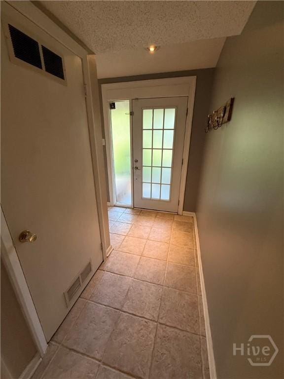 doorway to outside with a textured ceiling, light tile patterned floors, and baseboards