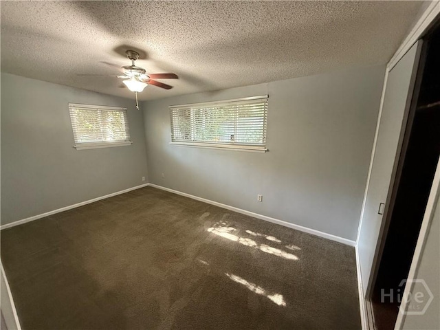 unfurnished bedroom featuring a textured ceiling, dark carpet, a closet, baseboards, and ceiling fan