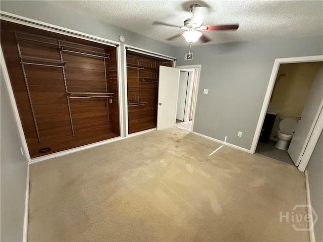 unfurnished bedroom featuring multiple closets, a textured ceiling, light colored carpet, baseboards, and ensuite bath