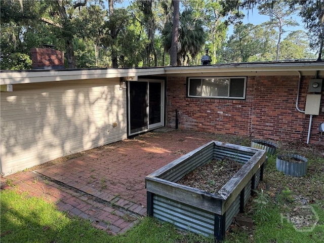 back of house featuring brick siding, a chimney, a vegetable garden, and a patio
