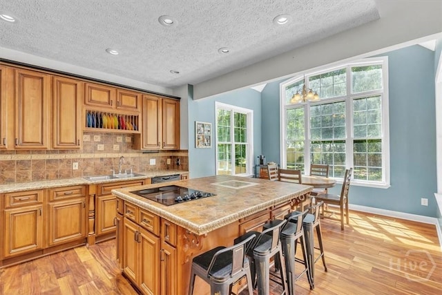 473 Kolic Helmey Rd, Guyton, GA 31312 - kitchen with black electric cooktop, a sink, light wood-style floors, a kitchen bar, and decorative backsplash